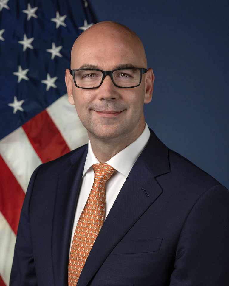 Jonathan Morrison, head of the National Highway Traffic Safety Administration, in black-framed glasses, a navy jacket and an orange patterned tie, in an official portrait in front of an American flag.